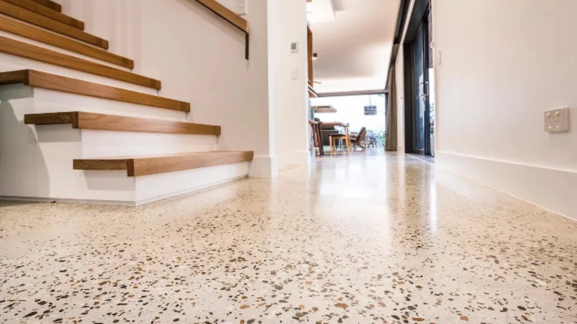 Polished terrazzo floor with warm-toned speckled aggregate beside a wooden staircase in an open-plan home