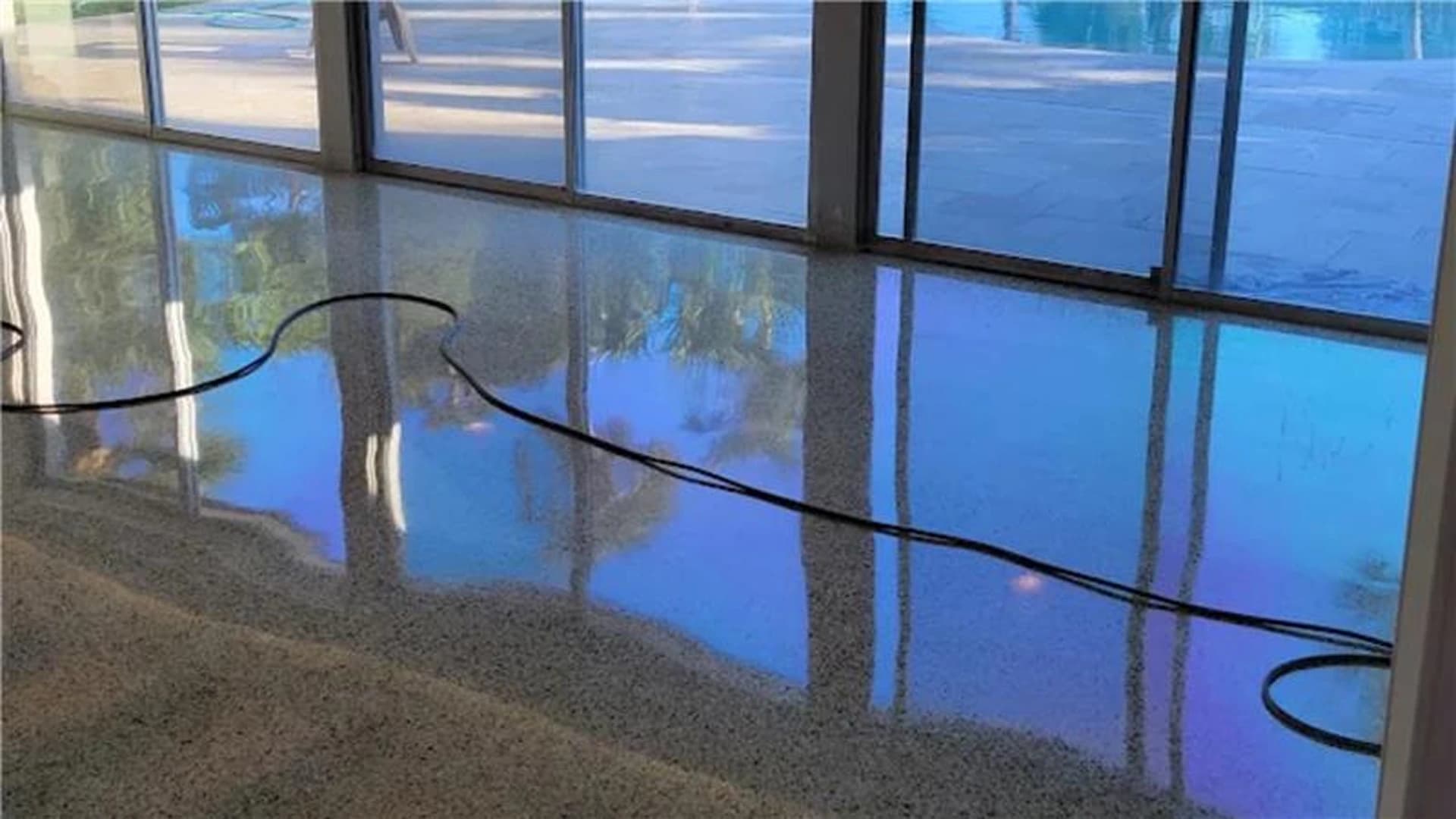 Restored terrazzo floor with an aggregate finish reflecting a pool and palm trees through floor-to-ceiling windows